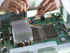 Close-up of a technician repairing a computer motherboard, focusing on microprocessor and heat sink.